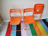 Four orange folding chairs arranged with two standing and two folded against the wall.