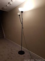 Black floor lamp with three branches and white frosted glass shades lit against a beige wall near stairs