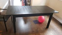 Black rectangular dining table in non-extended form, showing two solid legs on one side and wood floor beneath.