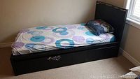 Single black wooden twin bed on carpet with mattress and pillow