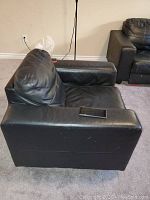 Side view of one black genuine leather armchair showing wide armrest and slightly creased seat cushion.