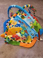 Full view of colorful ocean-themed baby play mat with padded structural arches and hanging plush fish toys