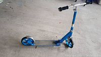 Two scooters, one with a wheel that needs replacement. Both blue and silver, adjustable handlebars with black grips.