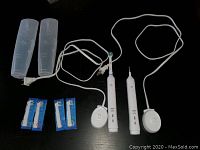 Two white electric toothbrushes with chargers, two transparent case covers, and four new replacement brush heads on a black surface, cords visible.