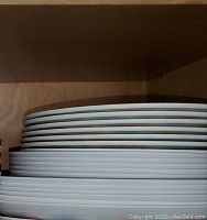 Stack of 12 white flat plates, 6 larger on bottom, 6 smaller on top, stored in cupboard