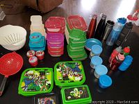 Photo showing multiple stacks of plastic food containers with colorful lids, character-themed containers, two plastic colanders, and assorted plastic and metal water bottles.