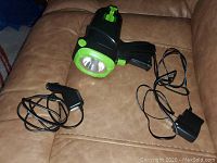 Power torch with two charging cables displayed on a brown leather couch, showing the torch's front light and cords.