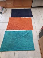 Three rugs laid out on the floor: navy blue, orange, and turquoise colors.