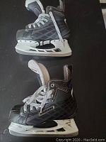 Side profile of black and gray Bauer hockey skates with white laces on black surface.