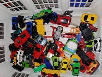 A group of various toy cars displayed tightly packed, showing a variety of colors, styles, and shapes including trucks, sports cars, and remote controllers.