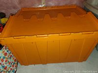 Orange plastic storage bin with hinged cover closed, showing the ribbed exterior and interlocking lid design.