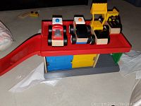 Image showing three wooden toy vehicles placed on top of a wooden garage playset with a red ramp and sliding blue and yellow doors beneath.