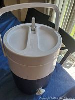 Side view of white lid and handle on dark gray base of Coleman beverage cooler