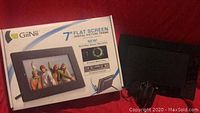 GiiNii 7-inch flat screen digital picture frame placed next to its original box, power adapter, and stand on a red surface.