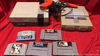 Photo showing NES console, SNES console, NES zapper light gun, and game cartridges on red background.
