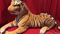 Full side view of large orange and black striped tiger plush lying down on red fabric background