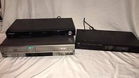 Photo of three devices stacked: top is Samsung DVD player, middle is Samsung DVD-VCR combo, bottom is JVC VCR player
