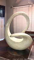 Frontal angled photo of large curved sculpture with mosaic mother of pearl tile texture on its surface, sitting on a round base, approximately 30x24 inches.