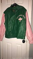 Full view of front of green and pink leather Alpha Kappa Alpha jacket hanging on hanger showing overall condition and style.