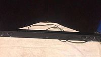 Front view of black LG soundbar placed on a textured light-colored surface with power cable visible.