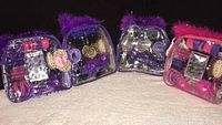 Two packaged girls hair styling accessory sets, one with purple trim and one with pink trim, shown on carpeted surface.