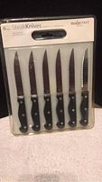 Photo of 6 steak knives in original sealed packaging by Mainstays, black handles with three rivets, serrated blades.