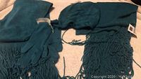 Teal scarf with fringe, matching gloves, and a hat laid out on fabric surface