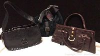 Three women's purses shown together: black embossed leather crossbody, dark brown crocodile texture handbag, black fabric shoulder bag.
