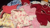 Photo showing multiple baby clothes in assorted colors and styles laid out, including sleepers, jackets, and onesies.