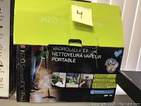 Box of H2O Steam FX Pro portable steam cleaner showing product branding and some features in French and English, emphasizing elimination of 99.9% bacteria and multiple attachments.
