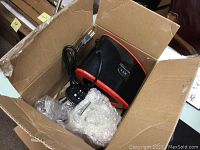 Black and red Homever slow juicer main unit inside a cardboard box with power cord and on/off switch visible.