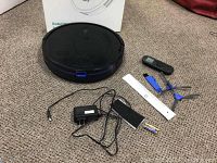 Full lot arranged on carpet: robotic vacuum, remote, charger, cleaning tool, spare filter, side brushes, batteries