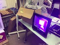 Two black HY brand LED flood lights emitting purple UV light, placed on table, one turned on, visible LED grid.