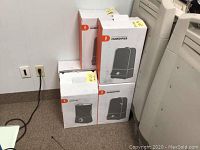 Six ultrasonic cool mist humidifiers in original retail boxes, some stacked on carpeted floor by white wall.