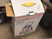 Baby walker box labeled 'Useful Baby Walker' with yellow handle on top, partially opened.