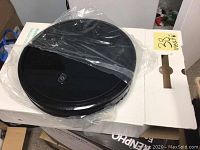 Photo of the Eufy RoboVac S11 in black, placed on top of packaging box wrapped in plastic.