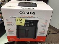 Front view of the closed and boxed Cosori 5.8 quart air fryer with brand name, model, and main features highlighted on the packaging.