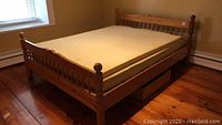 Queen pine bed frame assembled in a room with cannon ball style posts and spindle design headboard and footboard, foam mattress on top