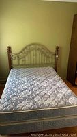 Front view of the queen bed set showing mattress with box spring underneath and metal and wood decorative headboard.