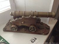 Side view of the brass cannon on its wooden carriage showing the metal wheels and mounting fixtures.