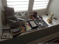 Wide view of the collection of items on window ledge showing trivets, containers, figurines, and smaller collectibles