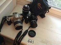 Photo of Canon EOS Rebel 2000 film camera with lens, Fujifilm FinePix S5000 digital camera with lens cap, Hanimar auto lens, and Lowepro camera bag on windowsill.