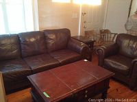 Overall view of brown leather sofa and matching armchair with coffee table in foreground