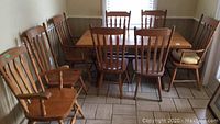 Full view of wooden kitchen table with all eight chairs around it, showing layout and general wear.