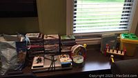 Table with stacks of DVD movies, children's toys including shape sorter and books visible in photo by window with blinds