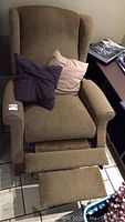 Front view of the brown wingback recliner chair with footrest extended and two throw pillows on seat.