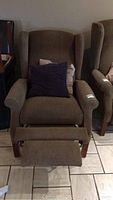 Front view of brown fabric recliner chair with footrest extended and two throw pillows on seat