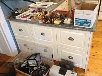 Photo of lower cabinet area showing a black Canon i900D printer, electronic accessories, and various household items.