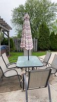 Wide shot of rectangular glass-top patio table with metal frame, umbrella inserted and six sling chairs around