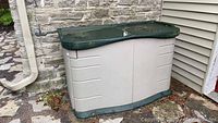 Front view of beige plastic storage box with green lid against stone and siding background